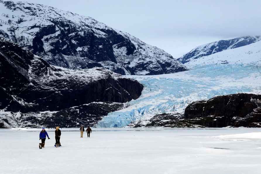 People walk on a frozen Mendenhall Lake, with Mendenhall Glacier...