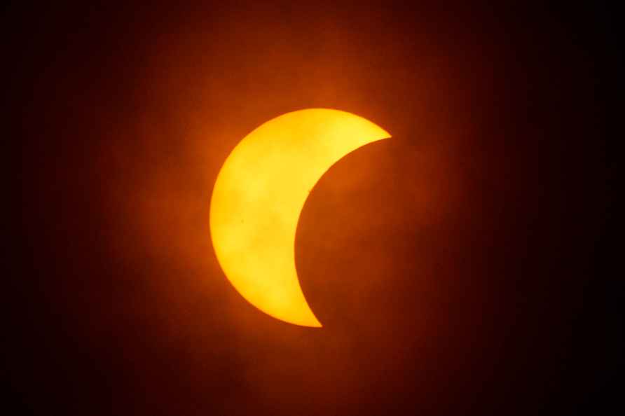 The moon partially covers the sun during a total solar eclipse, ...