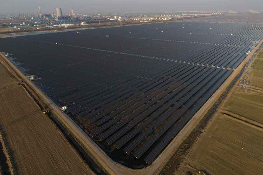 A solar farm stretches out near a chemical plant